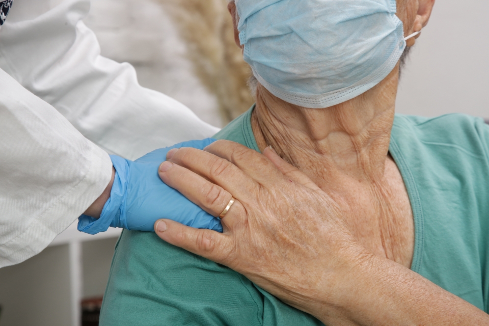 Masked nursing home resident with gloved hands of doctor 