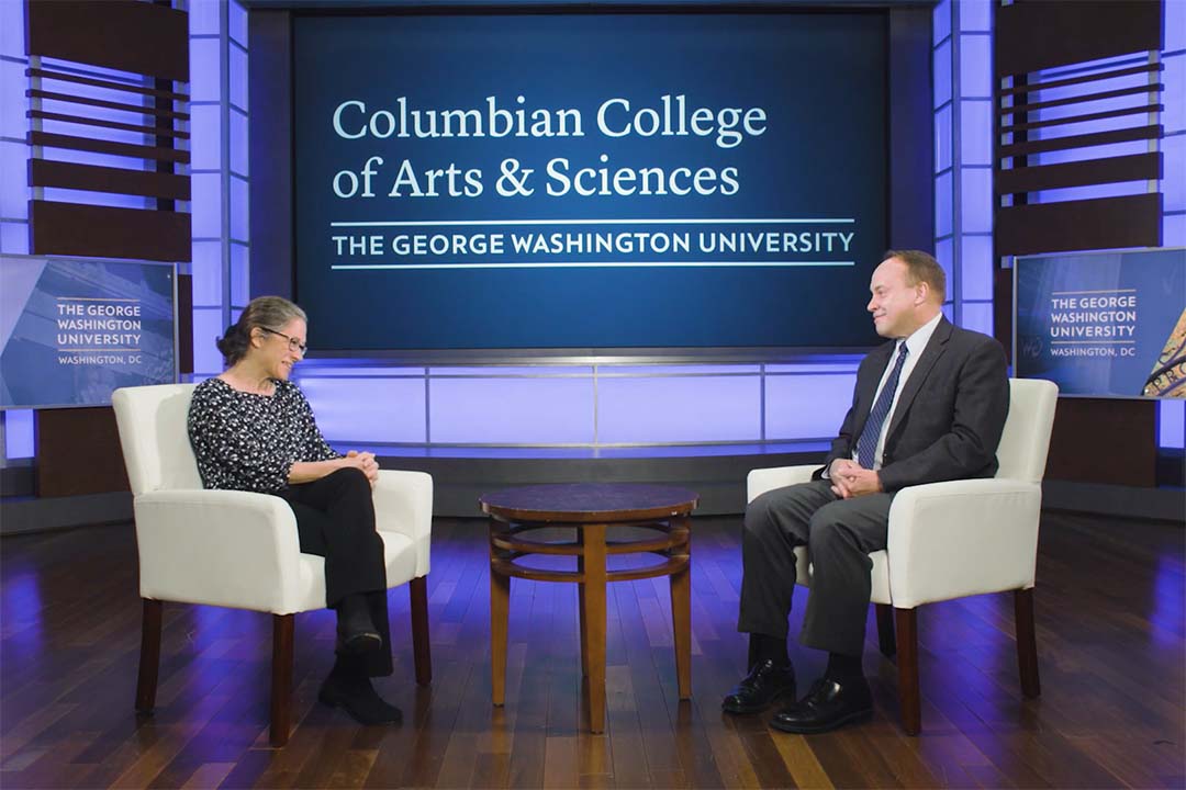 Sarah Binder and CCAS Dean Paul Wahlbeck seated on a stage talking with Columbian College signage behind them