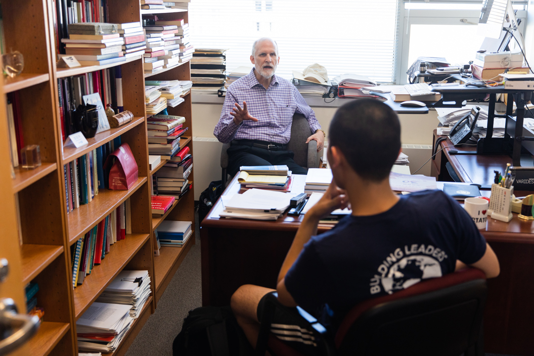 A GW political science professor sitting in a book-filled office across the desk from a student