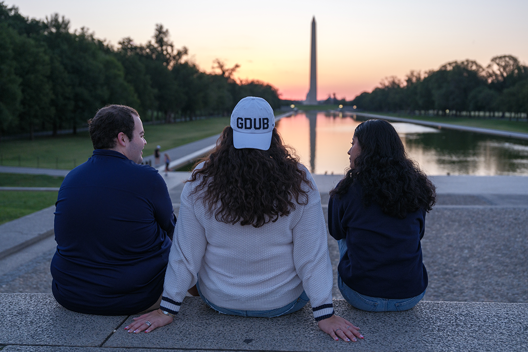 Three students looking out at the sunset behind the Washington Monument